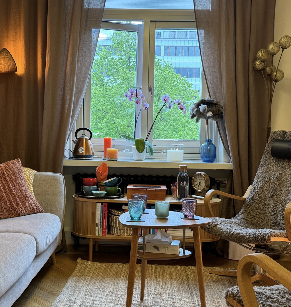 Katinkas mottagning vid Järntorget i Göteborg. Varm belysning, en soffa, två stolar, vackra glas på bordet och en utsikt genom höga fönster mot grönska.